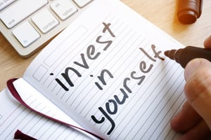 Man is writing invest in yourself in a note.